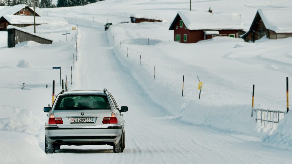 Auto rijdt op een besneeuwde weg, waar kou en gladheid het rijgedrag, remmen en voertuigcontrole beïnvloeden