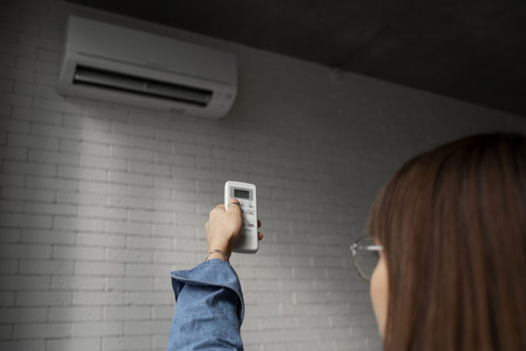 Vrouw bedient airco met afstandsbediening in huis.