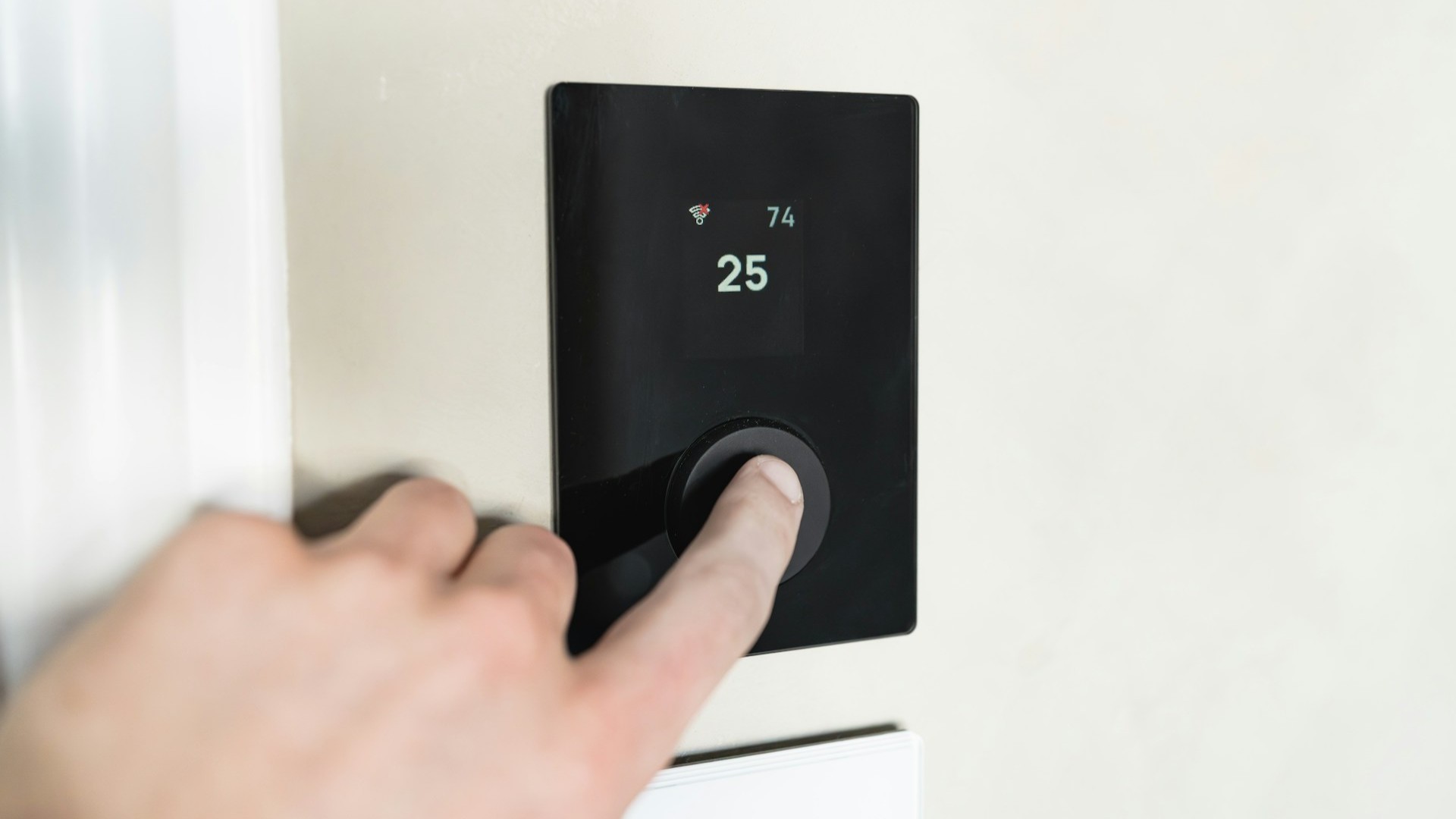 Hand bedient digitale slimme thermostaat op de muur, display toont 25 graden